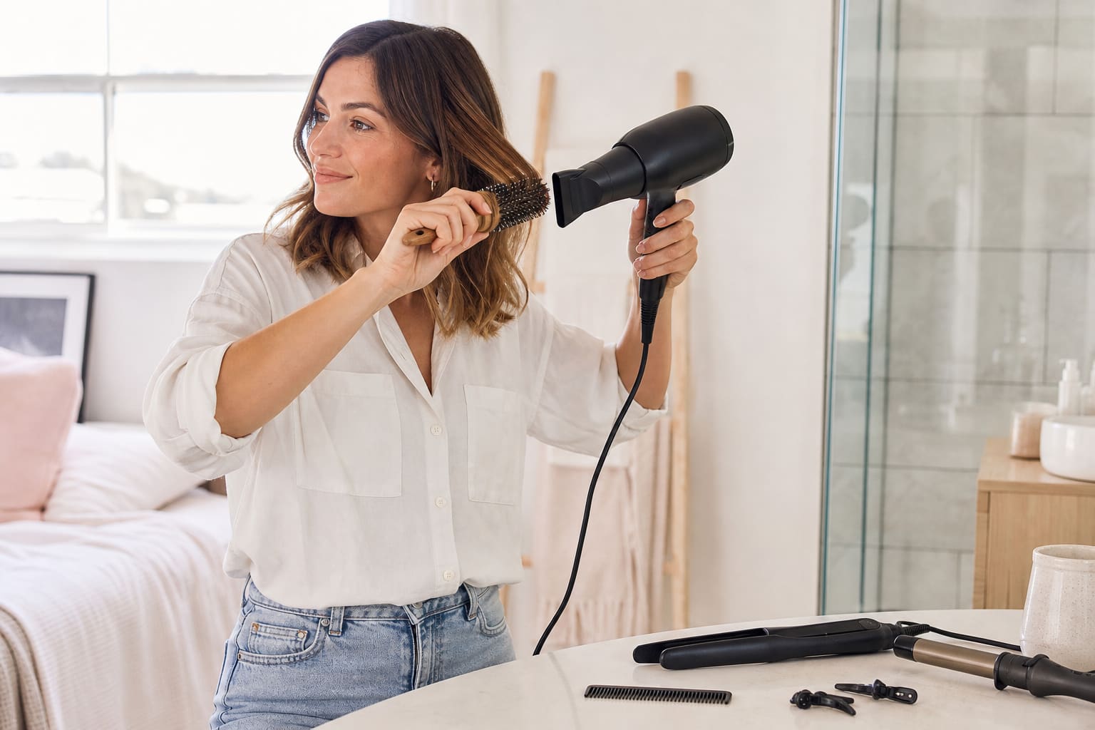 Femme utilisant un sèche-cheveux et une brosse ronde chez elle avec son matériel de coiffure
